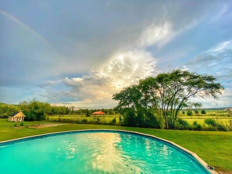 Backyard swimming pool after a thunderstorm with a rainbow appearing at sunset