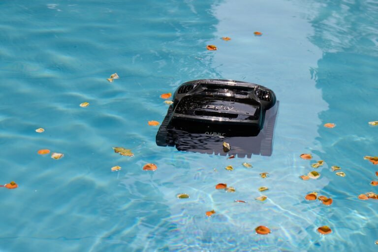 Robotic pool cleaner picking up fallen autumn leaves from the floor of a backyard swimming pool